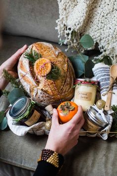 a person holding an orange in front of a loaf of bread and other food items