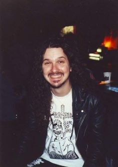 a man with long hair sitting down smiling