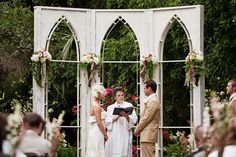 a couple getting married in front of an arch with flowers and greenery on it