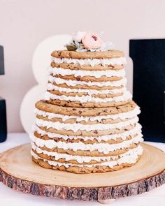 a wedding cake with white frosting and flowers on top sitting on a wooden slice