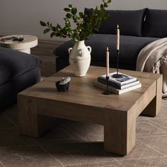 a living room with black couches and a coffee table in the middle, next to a plant