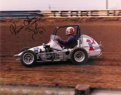 an autographed photo of a man driving a race car in the dirt with his helmet on