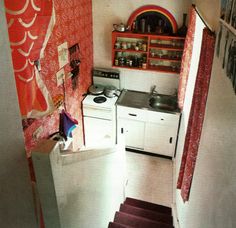 a small kitchen with red and white wallpaper on the walls, an open door leading to another room