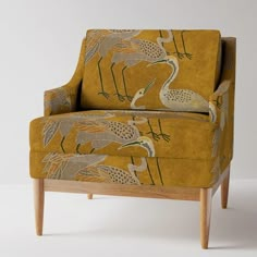 an upholstered chair with birds on the back and arms, sitting in front of a white wall