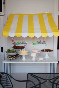 a yellow and white striped awning over a table with desserts on the table