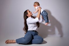 a woman sitting on the floor holding a baby up to her face with both hands