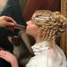 a woman is getting her hair done in front of a painting with a cat on it