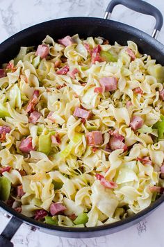 a skillet filled with pasta and ham on top of a marble countertop next to a spatula