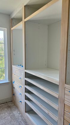 an empty room with shelves and drawers in the corner, next to a window that has blue tape on it