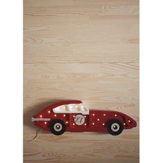 a red toy car with lights on the front and side, attached to a wooden wall