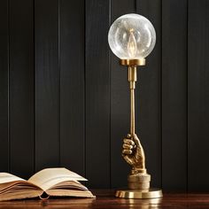 an open book on a wooden table next to a lamp with a hand holding a crystal ball