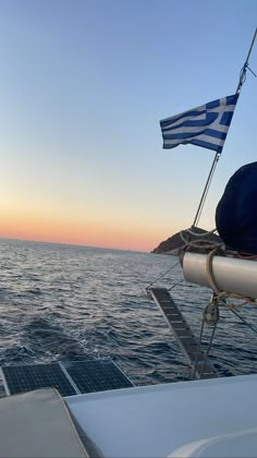 the sun is setting over the ocean and there are two flags flying on the boat