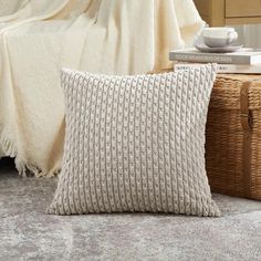 a white knitted pillow sitting on top of a bed next to a wicker basket