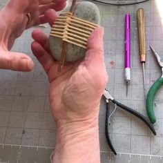 two hands are holding rocks and pliers next to some crafting supplies on a table