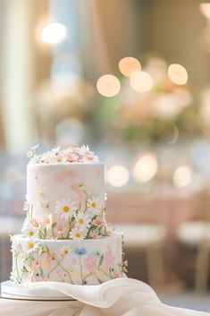 a three tiered cake with flowers on it sitting on top of a white table