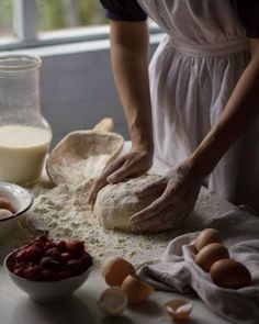 a person kneading dough on top of a table with eggs and other ingredients