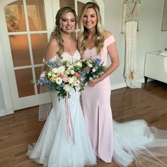 two beautiful women standing next to each other in front of a doorway holding bouquets