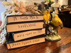 two yellow birds are sitting on top of some books that have been placed on a table