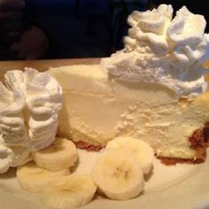 a white plate topped with a cheesecake covered in whipped cream and sliced bananas