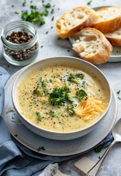 a bowl of broccoli cheese soup on a table with bread and spoons