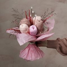 a person holding a pink bouquet with crocheted balls of yarn and knitting needles