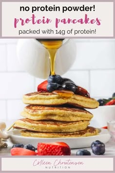 a stack of pancakes with blueberries, strawberries and honey syrup being poured on top