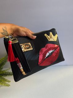 The Lola Luxe Clutch is a bold statement piece. Made with all-black fabric featuring black-on-black vertical stripes, this clutch stands out with sequin patches of red lips, lipstick, a crown, and a pair of eyes. This chic, playful design is perfect for those who love a mix of edgy and glamorous. Key Features: *All-black with subtle black-on-black stripes *Embellished with fun sequin patches: lipstick, lips, crown, and eyes *Roomy enough for daily essentials (phone, wallet, makeup) *Great for evening outings, parties, or as a stylish gift *Remake of the original Lola bag, a customer favorite.  Add a touch of glam and personality to your outfit with this unique, standout clutch. Here are some of the details of the bag  * Dimensions: 12 x 7 inches. * Black cotton print exterior.  * Cotton fa Stocking Fashion, Patch Bag, Sequin Patch, 2024 Christmas, Kissimmee, Iron On Patch, Daily Essentials, Phone Wallet, Stylish Gifts