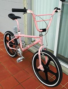 a pink and black bicycle parked on top of a brick floor next to a window