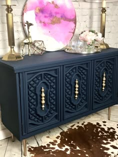 a blue sideboard with gold accents and a pink painting on it's wall