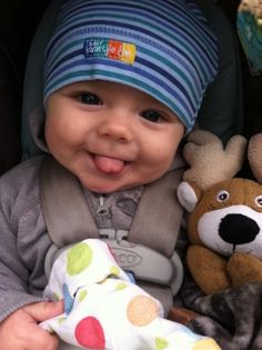 a smiling baby in a car seat next to two stuffed animals and a teddy bear