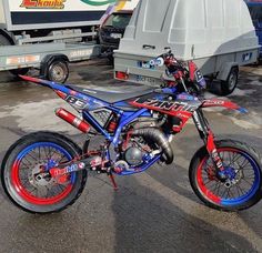 a red, white and blue dirt bike parked in front of a dumpster truck