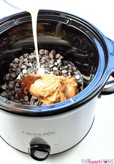 a slow cooker filled with chocolate chips and milk being poured into the crock pot