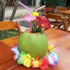 a green coconut sitting on top of a wooden table next to flowers and umbrellas