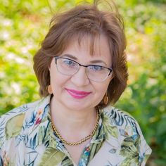 a woman with glasses is smiling at the camera in front of green grass and bushes