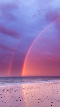 two rainbows in the sky over a beach at sunset with footprints on the sand