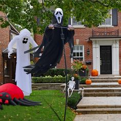 halloween decorations in front of a house with two ghostes and pumpkins on the lawn