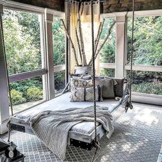 a swing bed with pillows and blankets in a room that has windows overlooking the trees