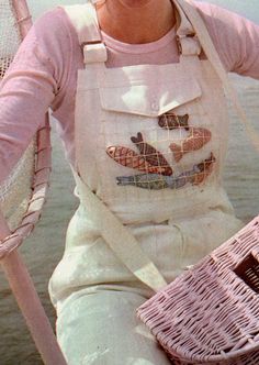 a woman in an apron is holding a basket and smiling at the camera while sitting on a boat