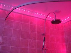 a shower head with pink lights on the ceiling and tiled walls in a bathroom setting