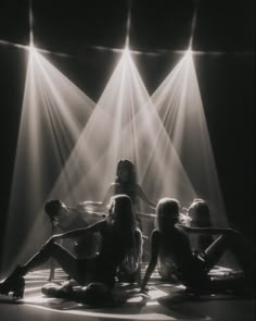 three women are sitting on the floor in front of spotlights with their legs crossed