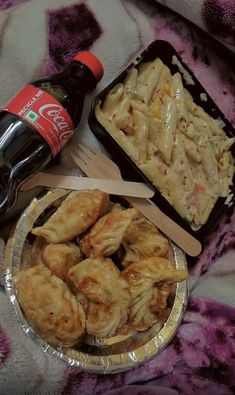 some food is sitting on a bed next to a bottle of coke and a fork