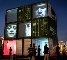 people are standing outside in front of a building with large containers on it's sides