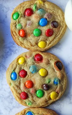 three cookies with m & m's on them sitting next to a bottle of milk