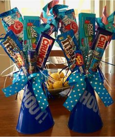 two blue vases filled with candy sitting on top of a wooden table next to a bowl of fruit