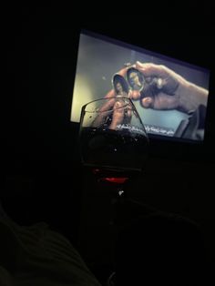 a person holding a glass of wine in front of a tv with the image of two hands on it