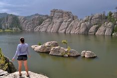 a woman standing on top of a rock next to a lake