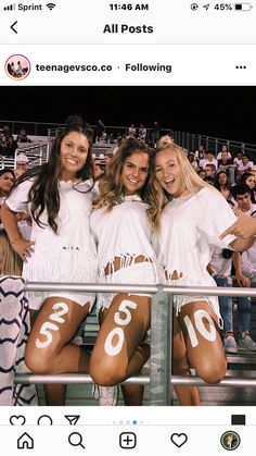 three women in white outfits posing for a photo at a sporting event with numbers painted on their legs