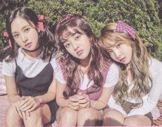 three young women sitting next to each other on top of a pink blanket covered ground