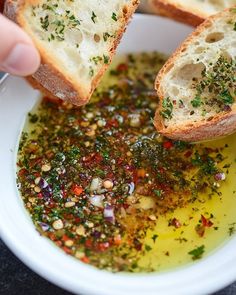 someone is dipping some bread into a bowl of olive oil with herbs on the side