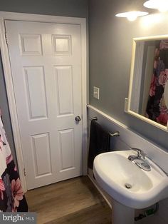 a white sink sitting under a bathroom mirror next to a doorway with a flowered shower curtain